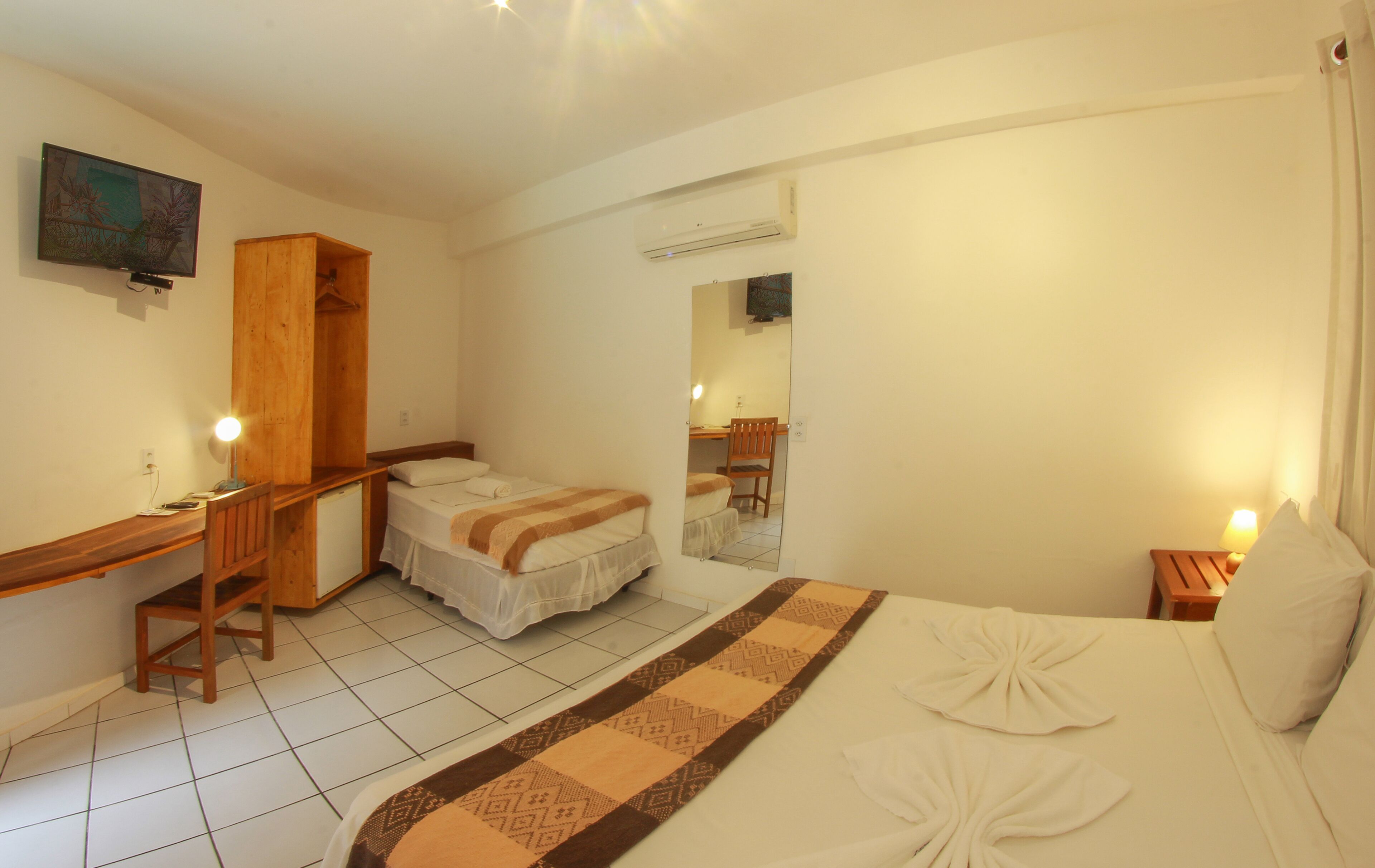 A hotel room with a bed, a desk, a chair, a wardrobe, and a mirror.
