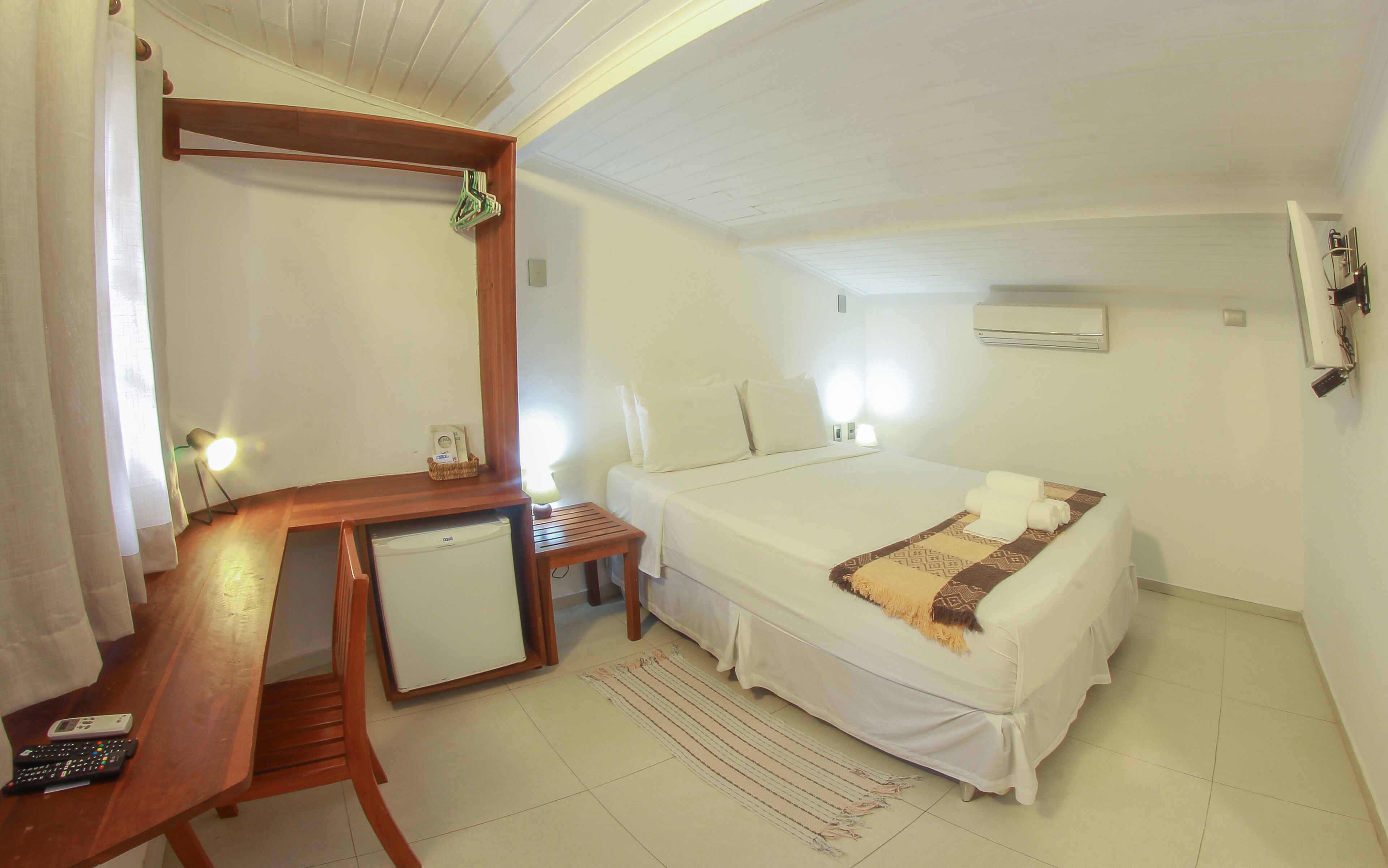 Een hotelkamer met een bed, een bureau met stoel, een kleine tafel, een spiegel en een airconditioning.