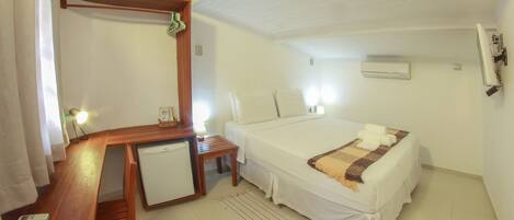 Een hotelkamer met een bed, een bureau met stoel, een kleine tafel, een spiegel en een airconditioning.