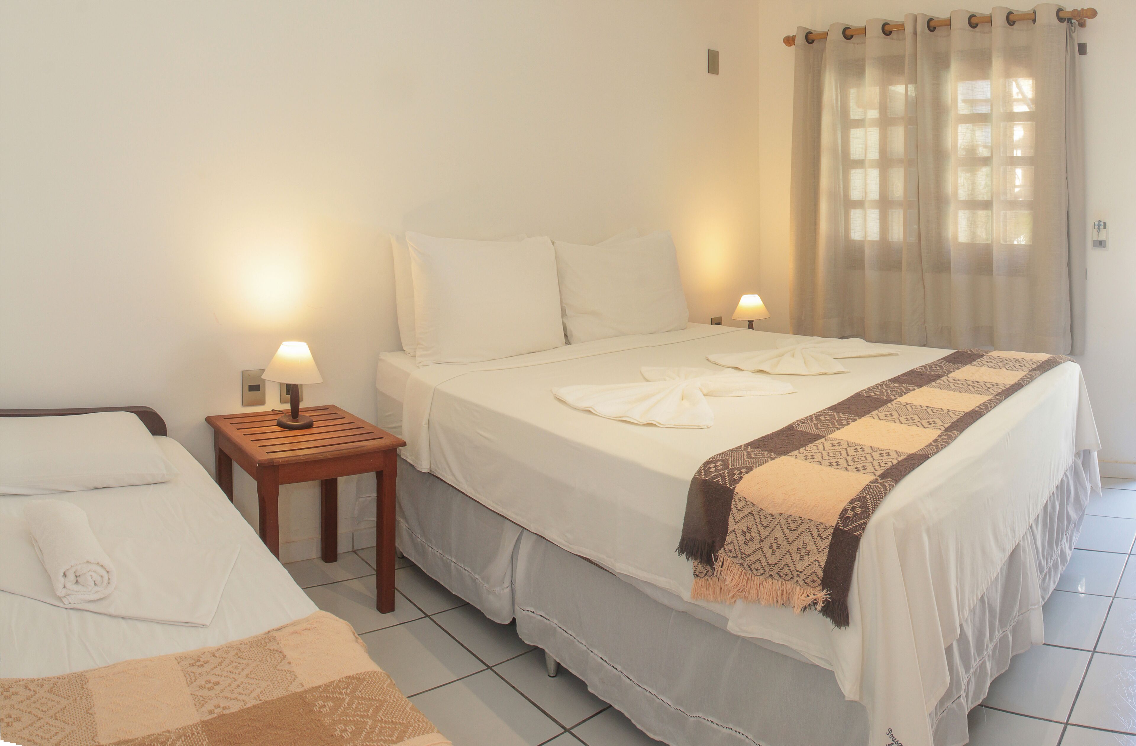 A hotel room with a bed, a nightstand, a lamp, and a window with curtains.
