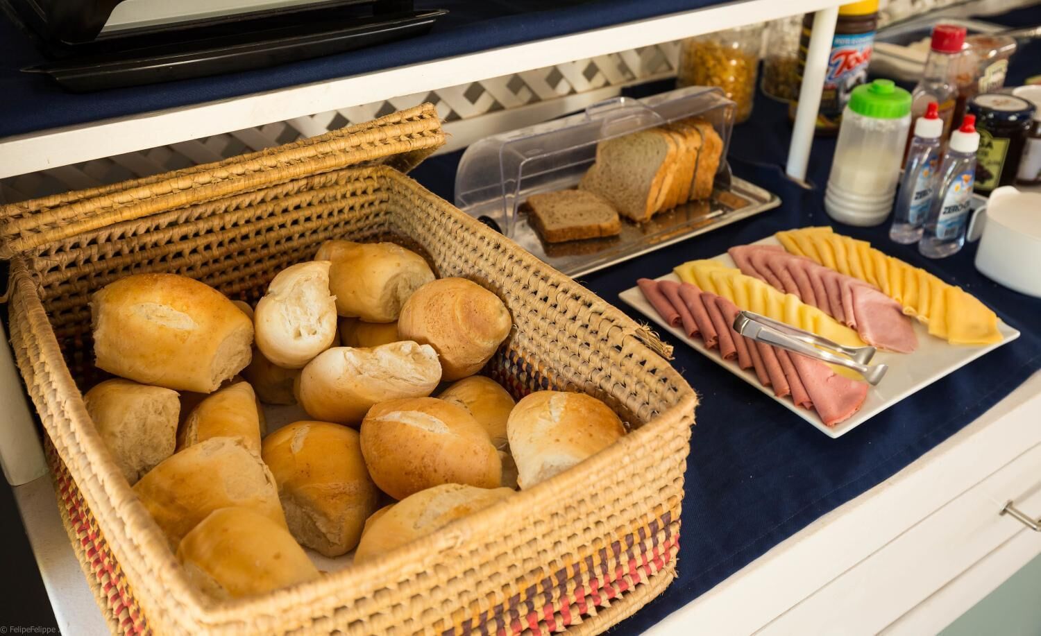 A basket of bread rolls and a plate of sliced meats on a counter.