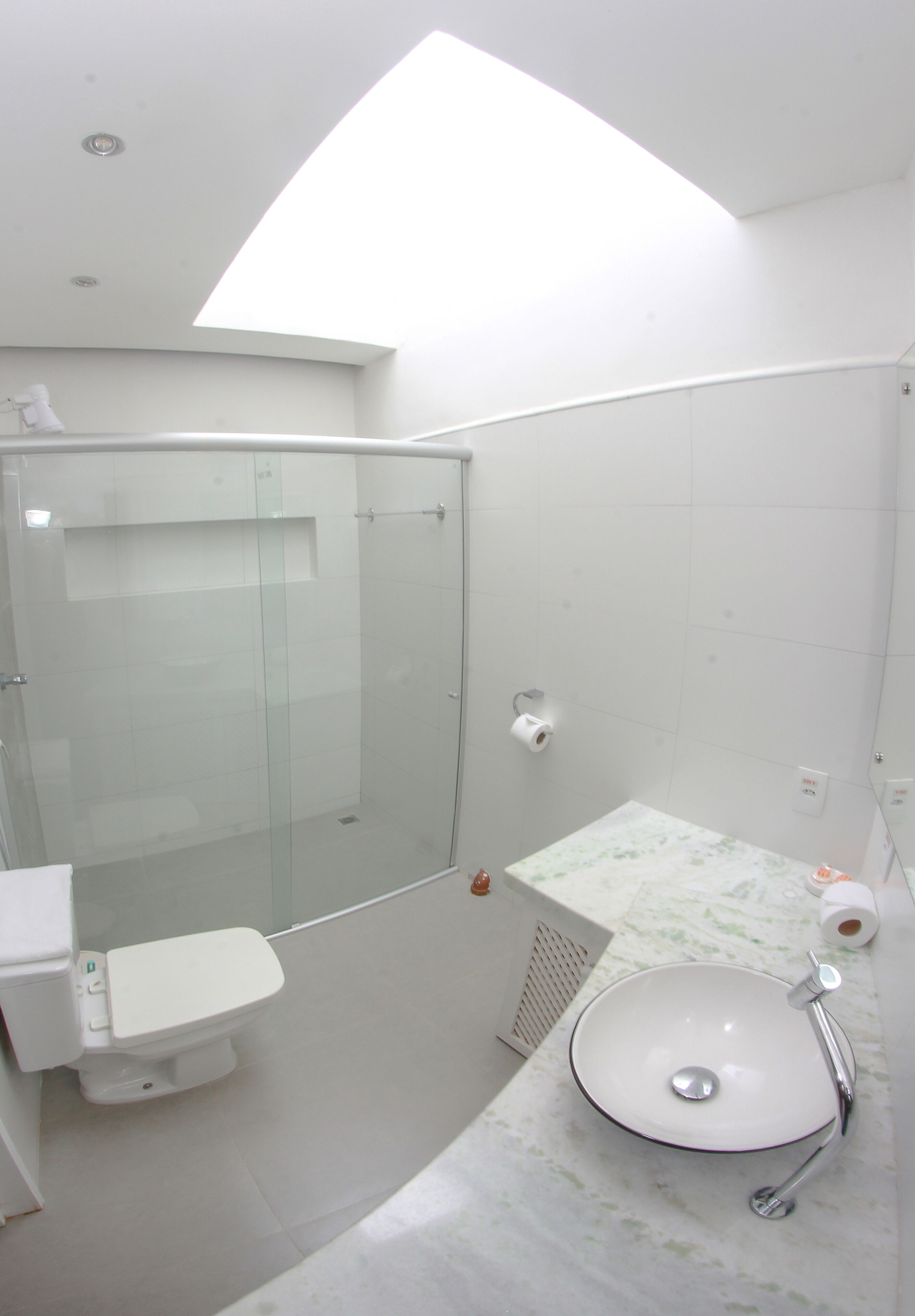 Un baño moderno con ducha envuelta en vidrio, inodoro blanco y lavamanos con encimera de mármol.