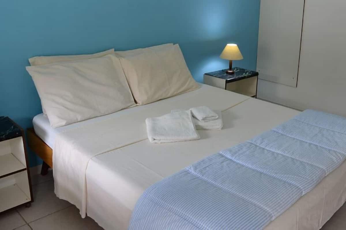 A neatly made bed with white linens, a bedside lamp, and a small bedside table with a lamp.