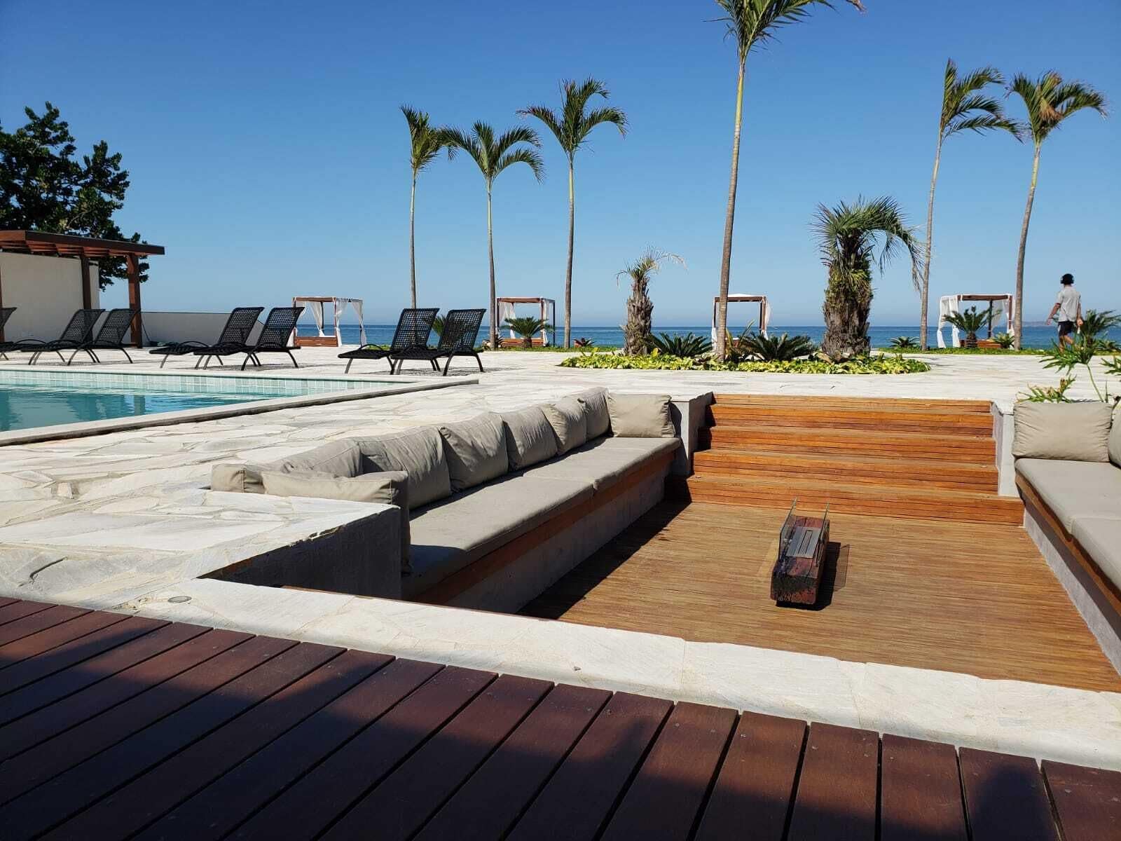 A poolside area with lounge chairs, a wooden deck, and palm trees.