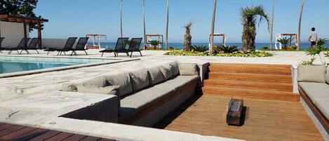 A poolside area with lounge chairs, a wooden deck, and palm trees.