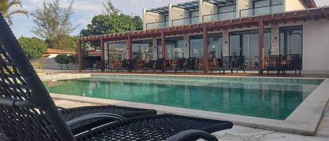 A pool area with lounge chairs and a building with large windows.