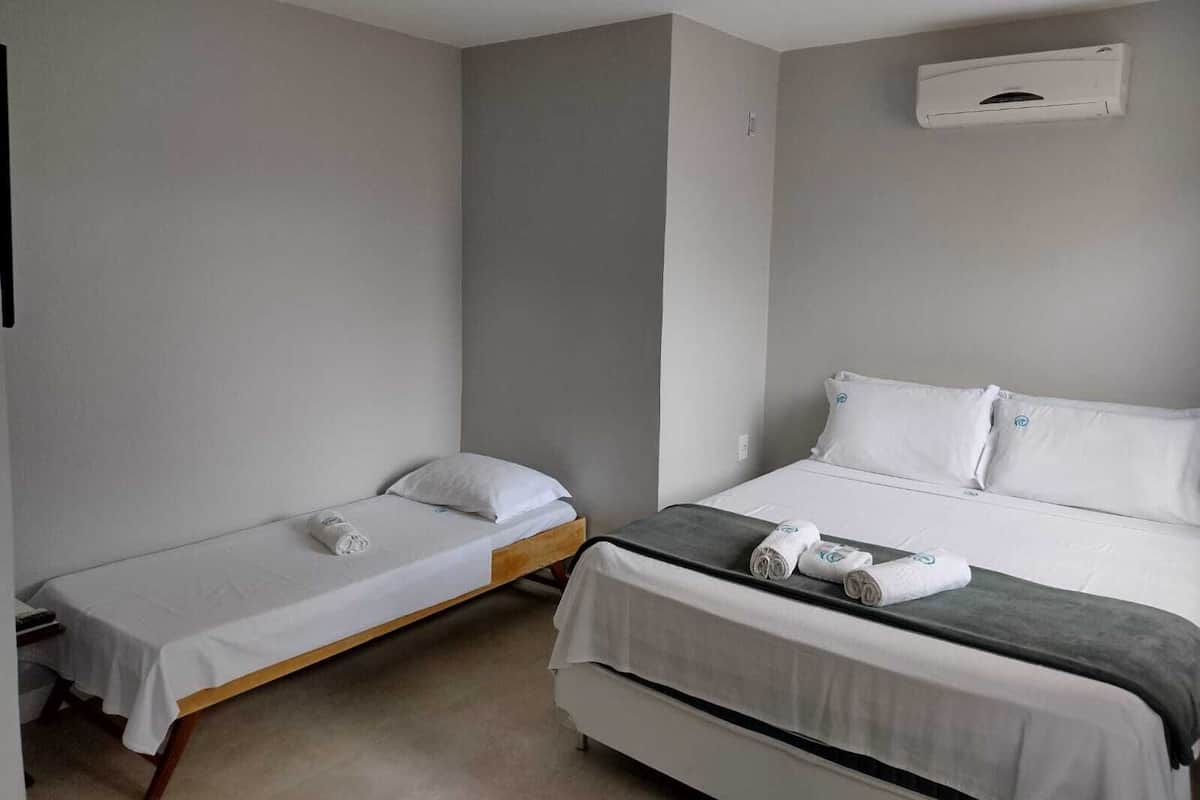 A room with two beds, one single and one double, both with white linens and pillows. There is a small table with a remote control and a phone.