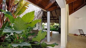 A covered outdoor area with large plants, a thatched roof structure, and a white pillar. - Instyle Residences at Seahorse Ranch Villa 118 (Cabarete)