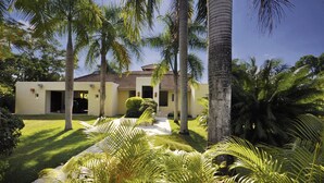 A two-story house with a tiled roof, surrounded by lush greenery and palm trees. - Instyle Residences at Seahorse Ranch Villa 118 (Cabarete)