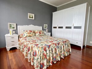 Un dormitorio con edredón estampado con motivos florales, un armario blanco y una mesita de noche con cajones.