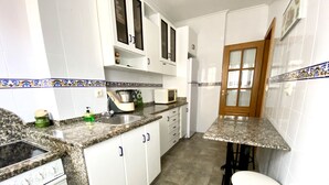 Una cocina con gabinetes blancos, encimeras de granito, estufa, microondas y pileta.