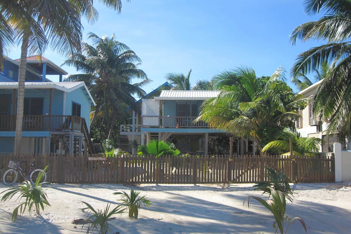 A beachfront property with multiple-story buildings, a wooden fence, and palm trees.