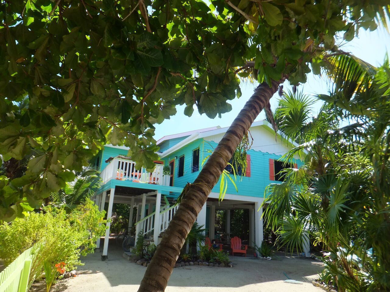 A two-story house with a porch and a small deck, surrounded by tropical vegetation.