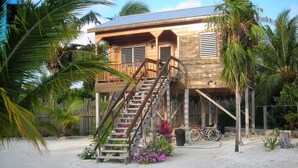 A wooden house with a staircase leading to a balcony, surrounded by palm trees and a bicycle. - Caye Caulker Vacation Homes (Caye Caulker)