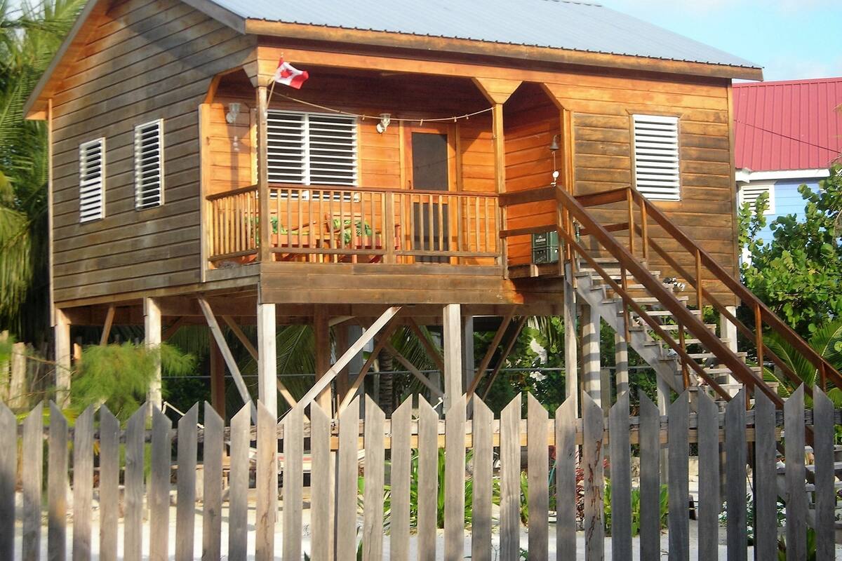 A wooden house with a balcony, a flag, and a staircase leading to the main entrance.