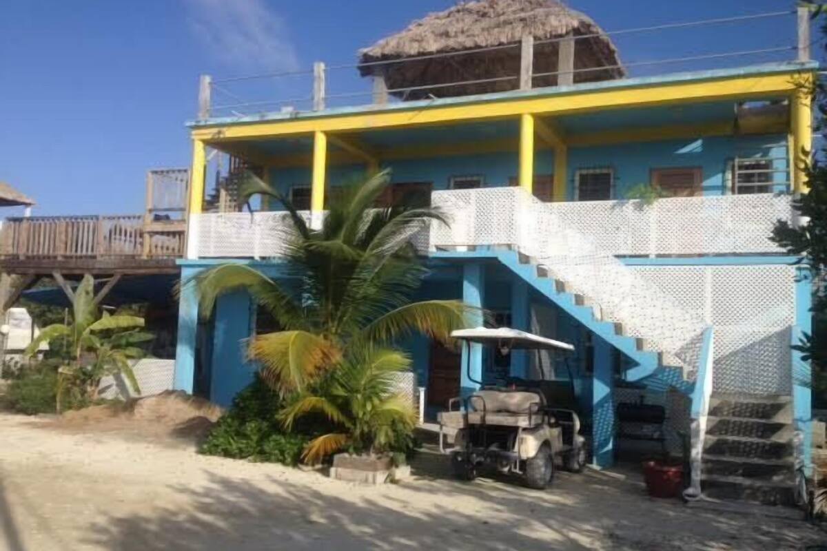 A two-story building with a blue and yellow facade, a thatched roof, and a staircase leading to the upper level.