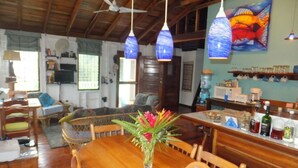 A wooden dining table with chairs, a vase of flowers, and hanging blue lamps. - Caye Caulker Vacation Homes (Caye Caulker)
