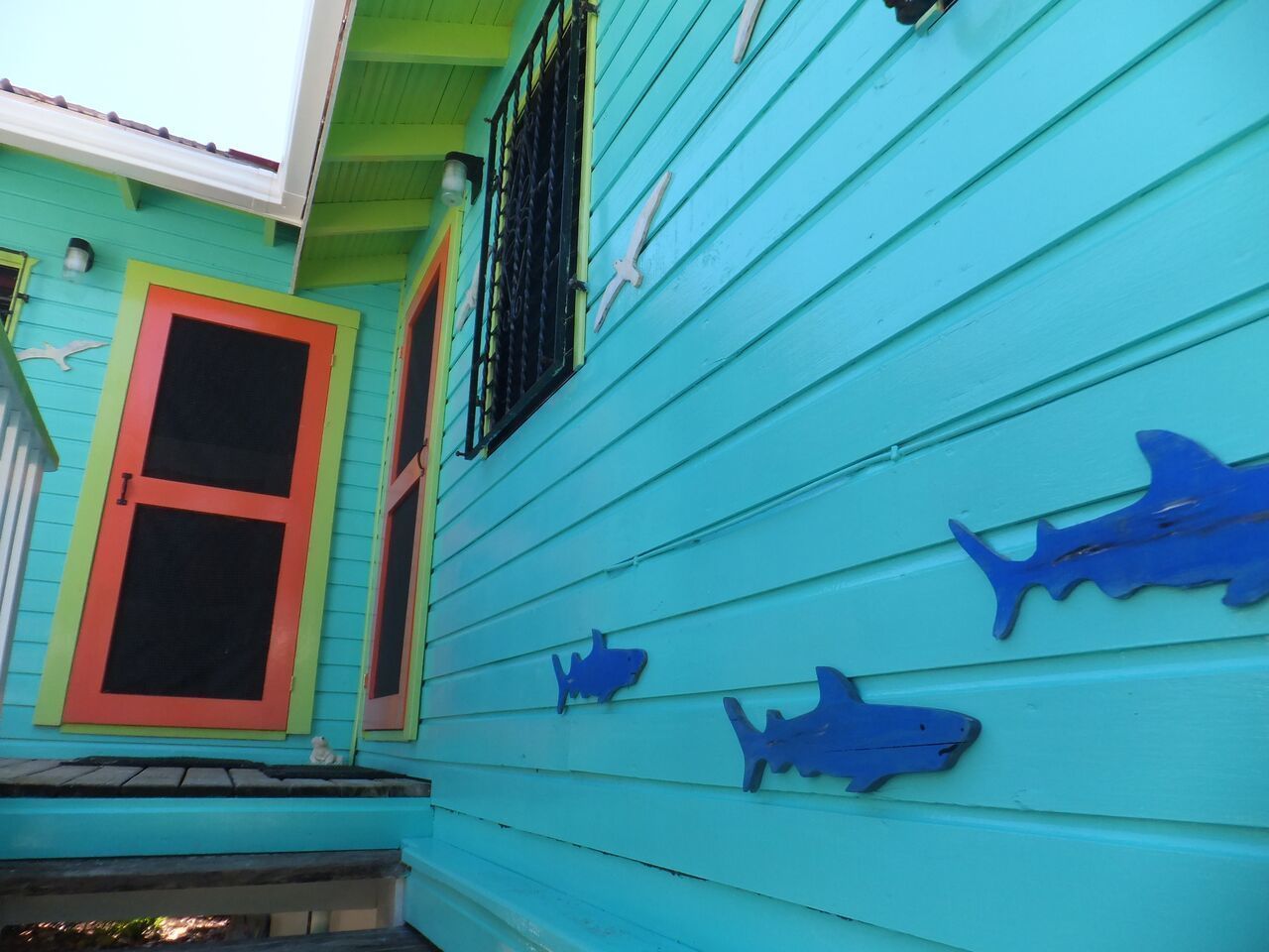 Una casa turquesa con ventanas de marco rojo y recortes de tiburones en el revestimiento.