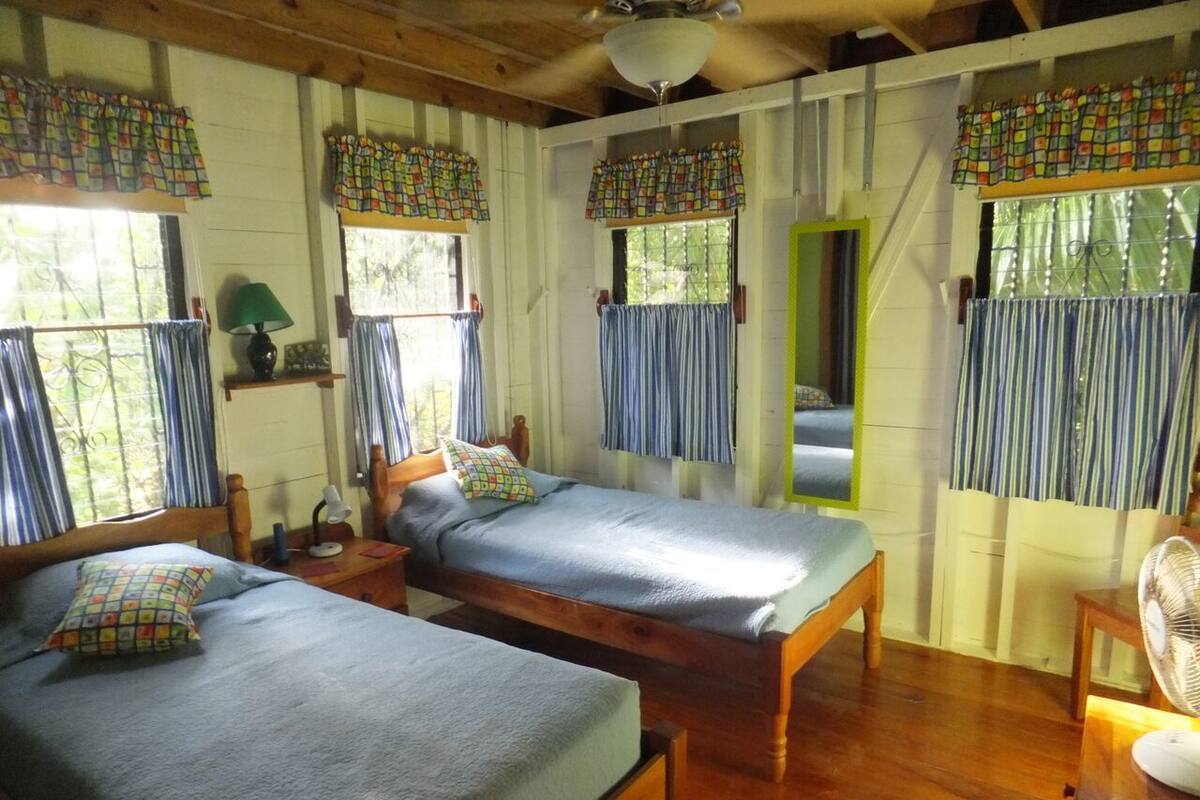 A room with two wooden beds, a nightstand, a lamp, and a fan.