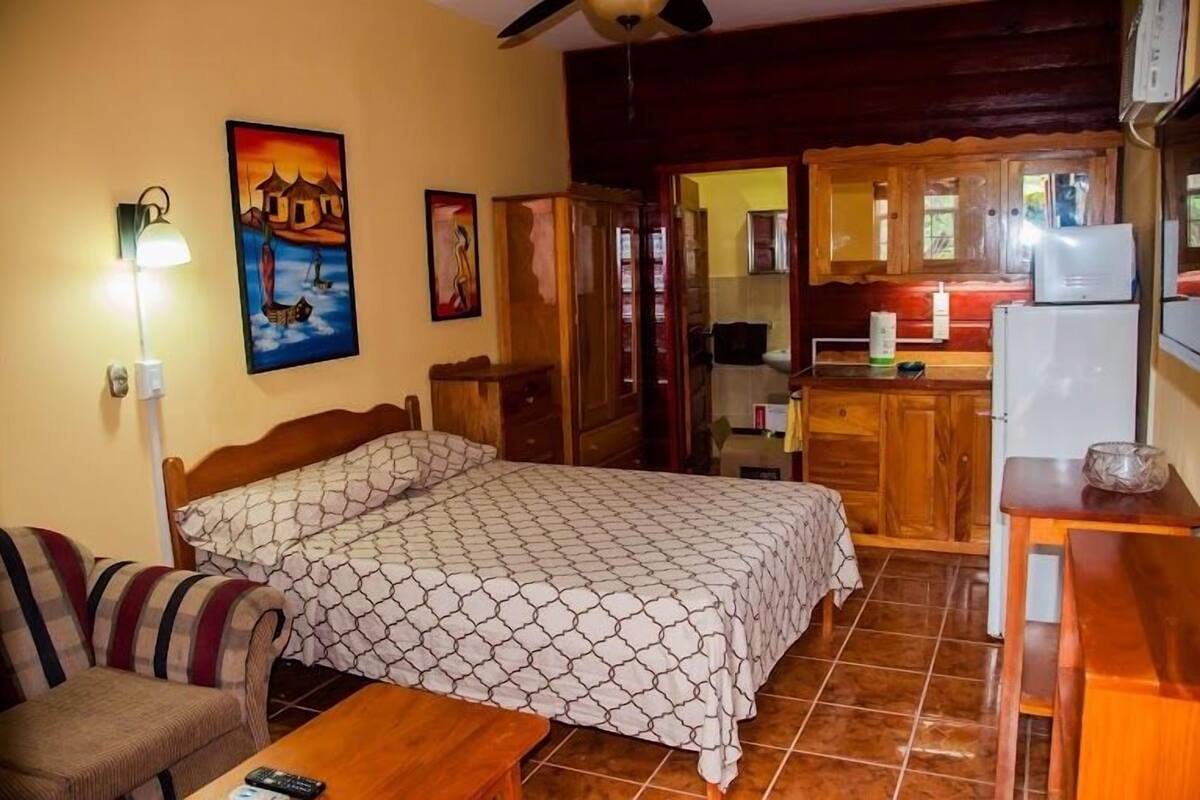 A bedroom with a bed, a wooden dresser, a nightstand, a lamp, and a painting on the wall.