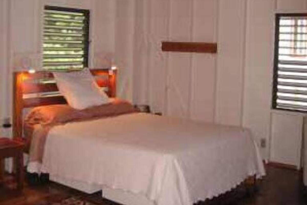 A bedroom with a wooden ceiling, a bed with white bedding, a nightstand, and a window with blinds.