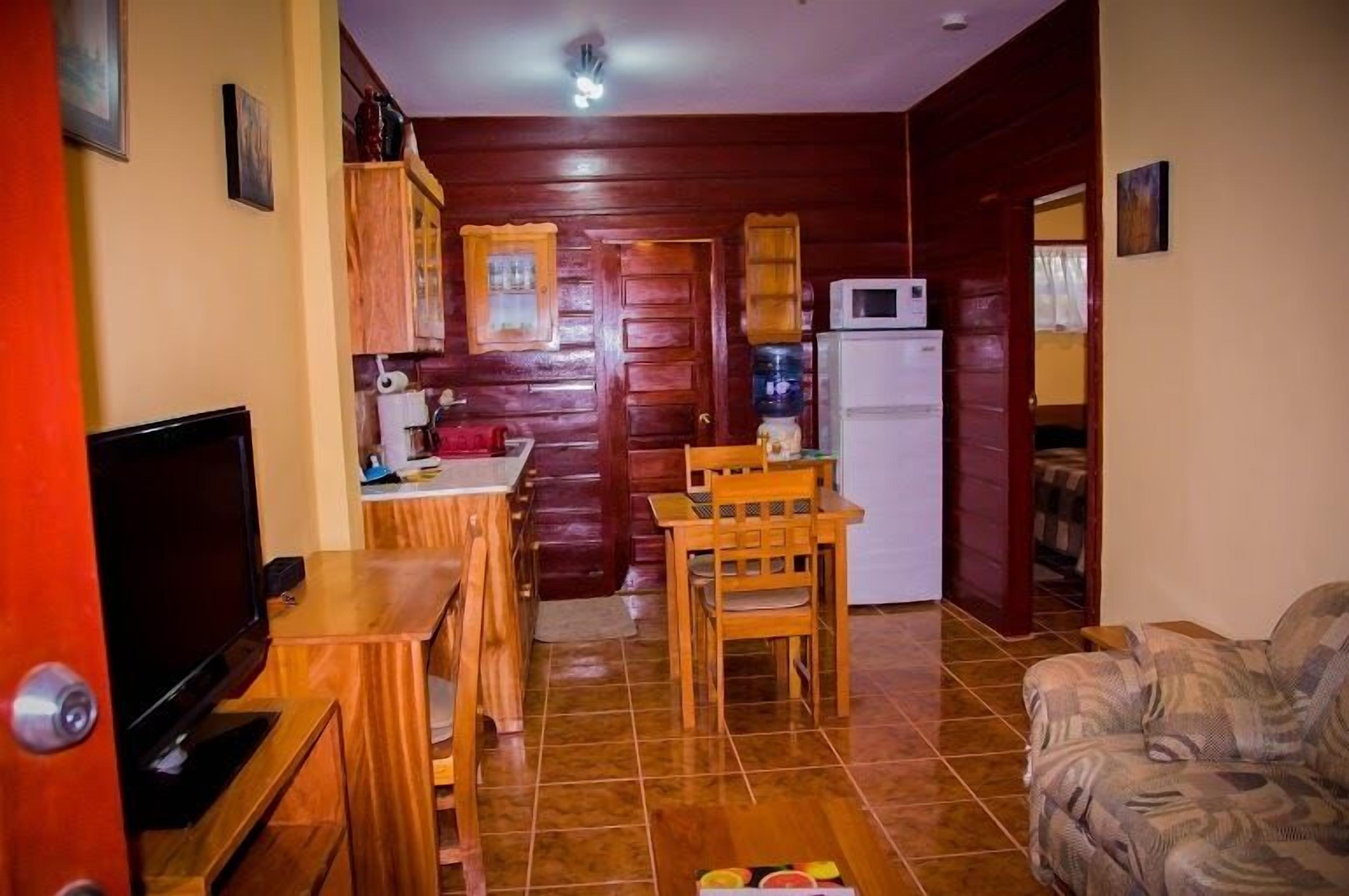 Um espaço de estar compacto com televisão, mobiliário de madeira, cozinha com micro-ondas e sofá.