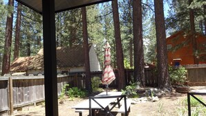 Un espace extérieur abrité, doté d’une table de pique-nique et d’un parasol, entouré de grands arbres et d’une clôture en bois.
