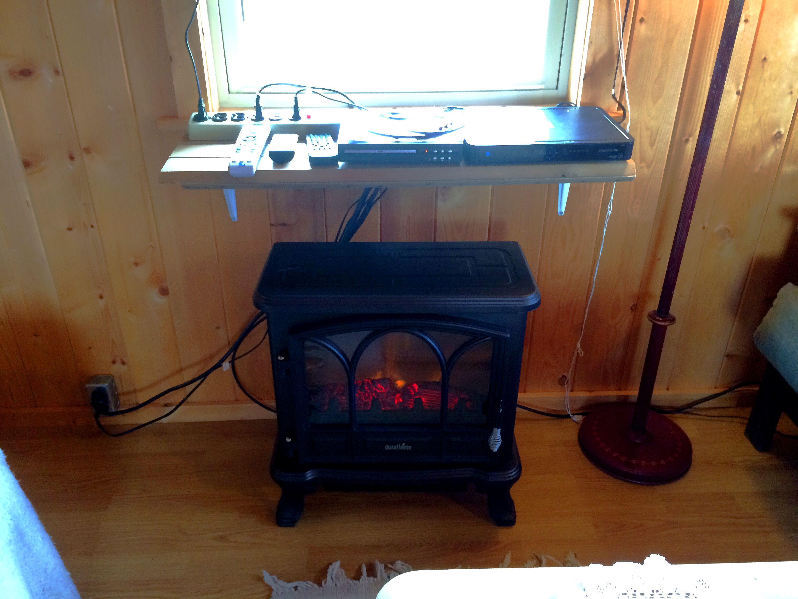 A room with a wooden interior, a black stove, a window, and a desk with electronic devices.
