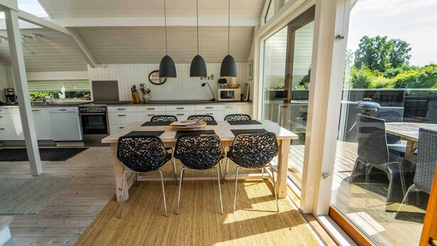 Une cuisine moderne dotée d’un grand îlot central, de luminaires suspendus et d’un coin repas avec des chaises en osier.