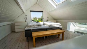Une chambre avec un plafond en pente, une grande fenêtre, un lit avec des oreillers, une table de chevet et un banc.