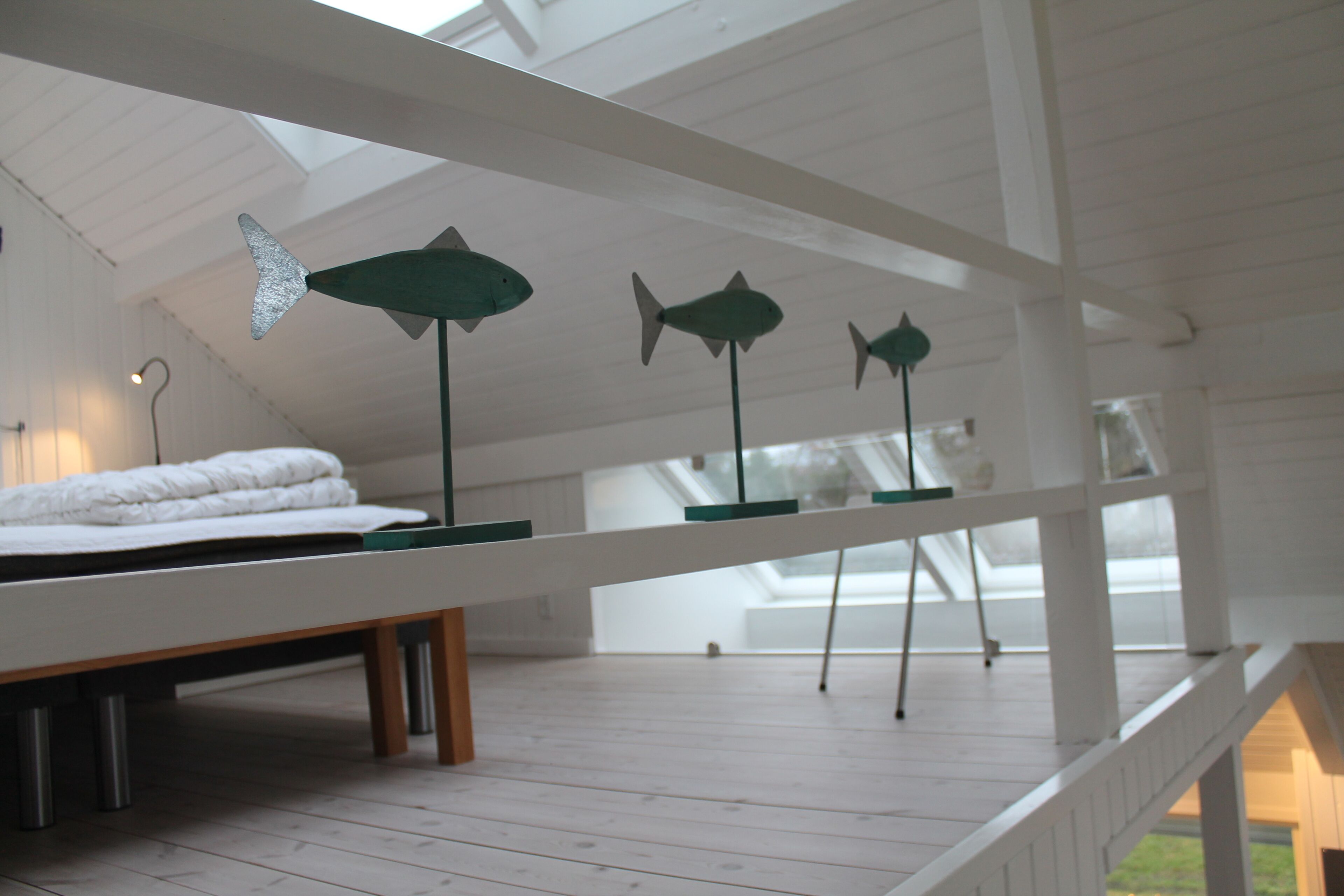 A bedroom with a bed, a desk, and three fish-shaped sculptures on the ceiling.