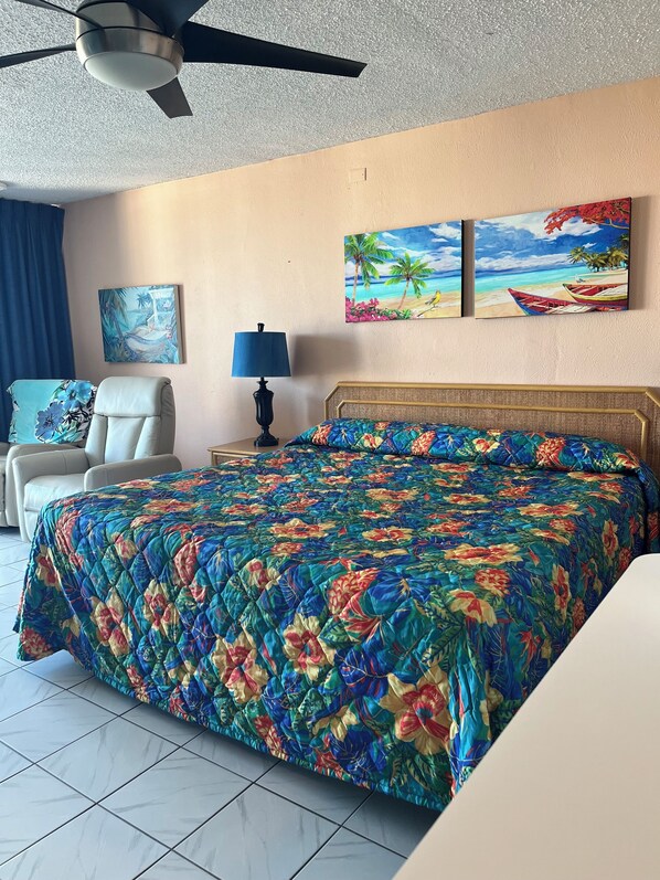 A hotel room with a bed, a chair, a ceiling fan, and two wall paintings.
