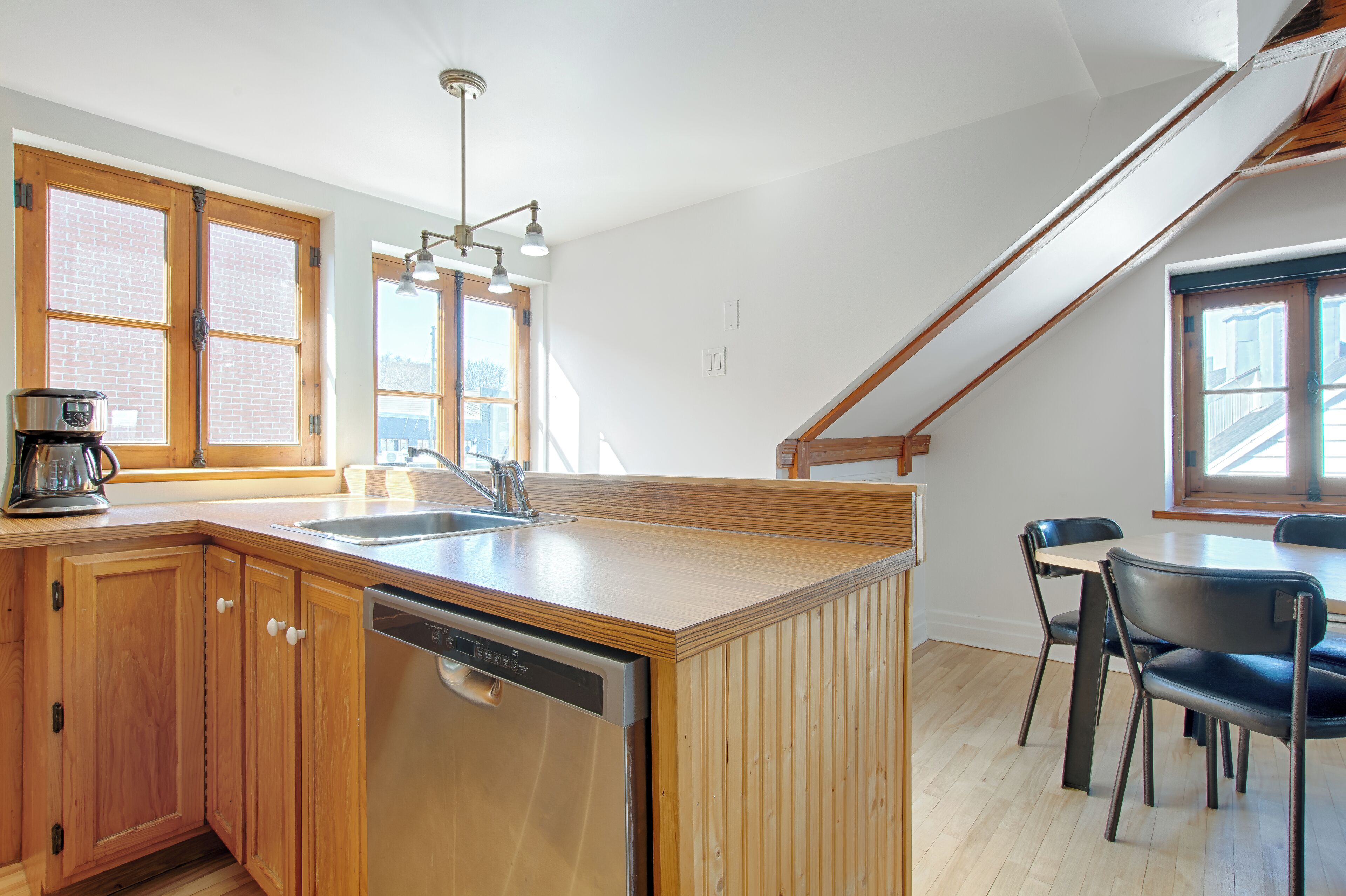 A kitchen with wooden cabinets, a dishwasher, a coffee maker, and a dining area with chairs and a table.