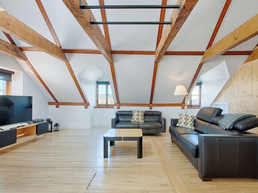 Un loft espacioso con vigas de madera a la vista, un televisor de pantalla plana grande, un sofá de cuero y una mesa de centro de madera.