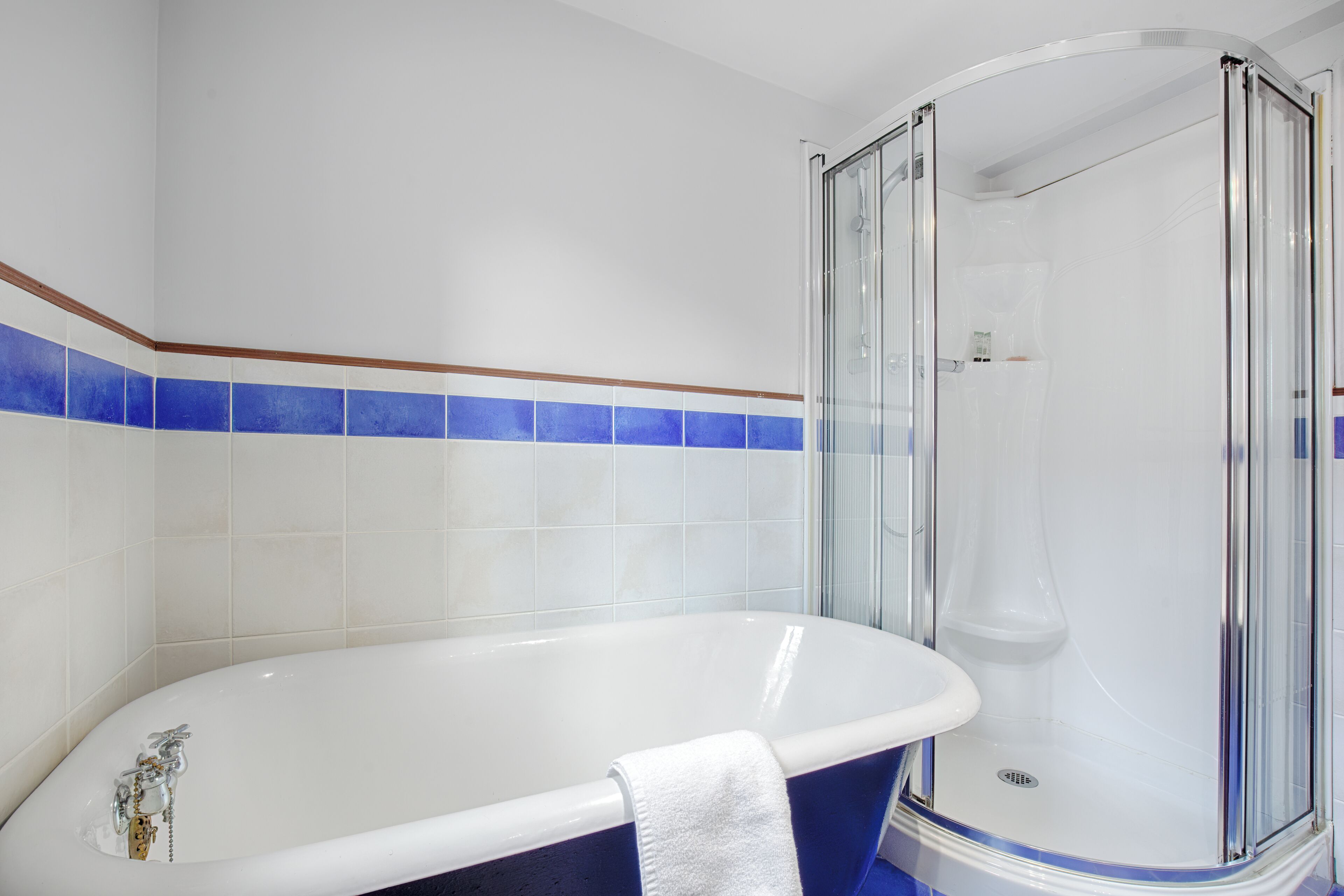 Un baño con bañera, ducha envuelta en vidrio y paredes de azulejos azules.