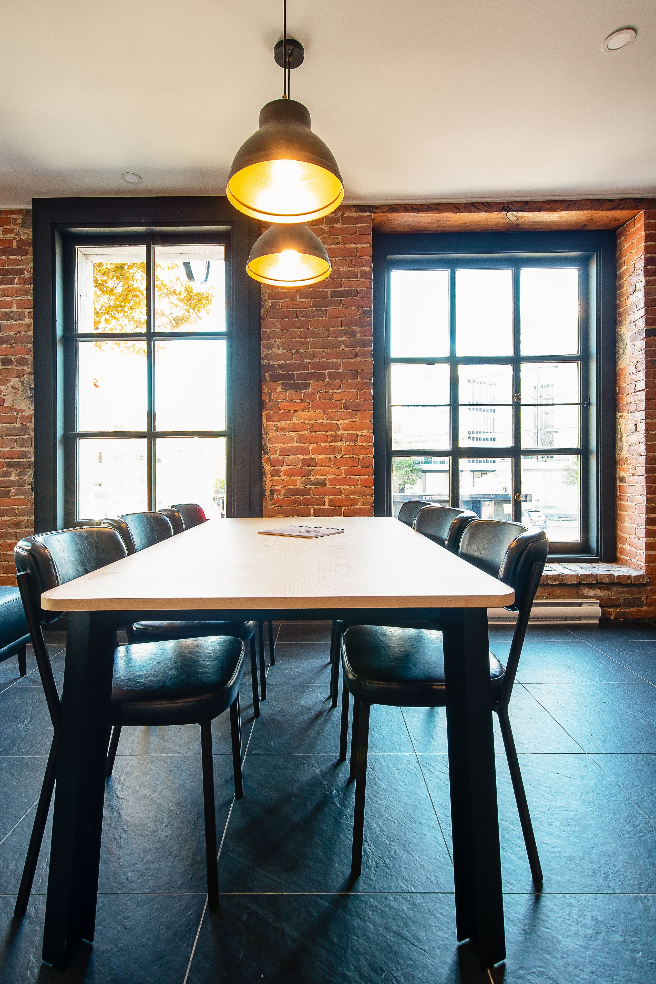 A conference room with a large table, black chairs, and a hanging light fixture.