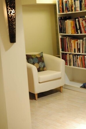 A modern living room with a white armchair, a bookshelf filled with books, and a patterned cushion.