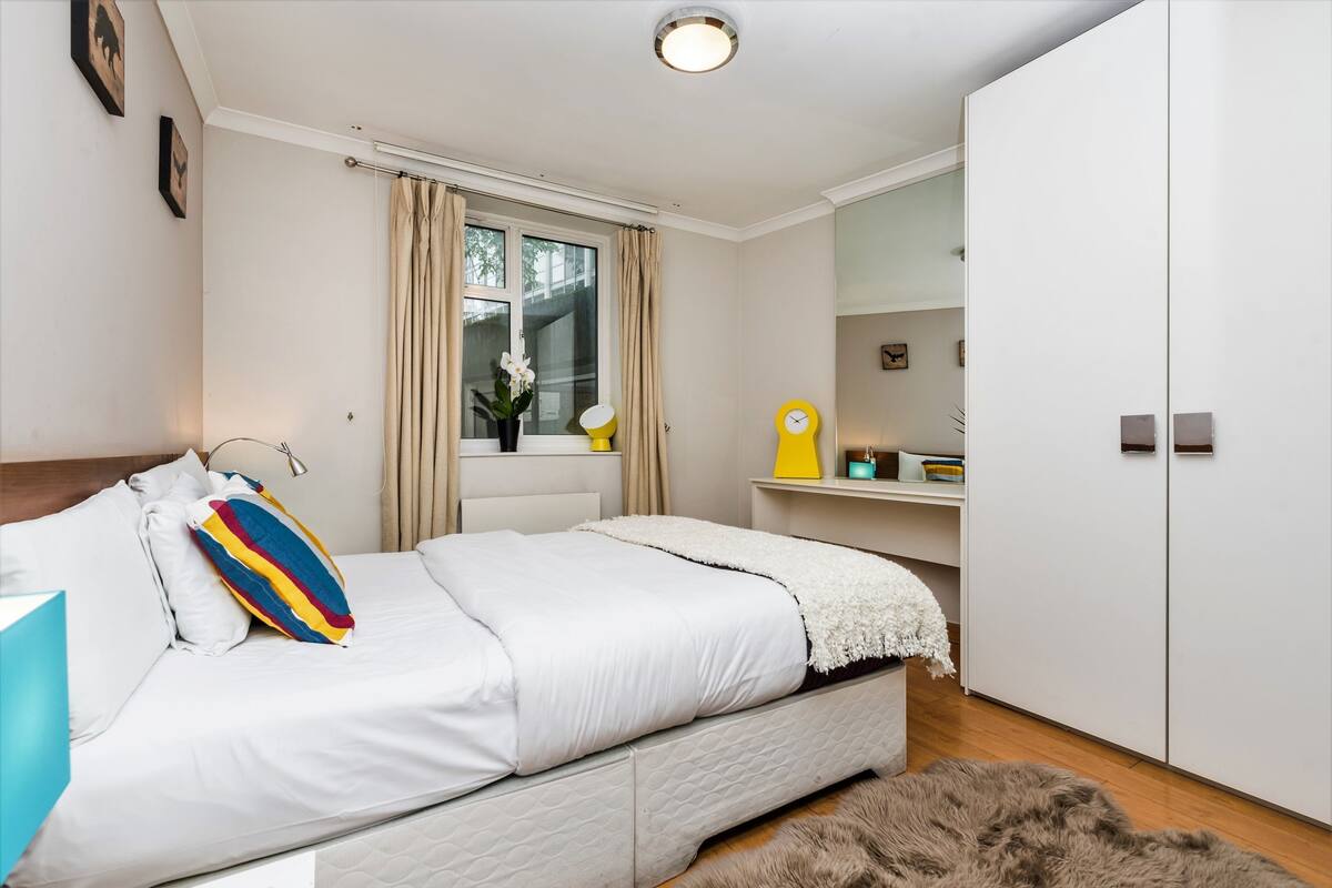 Une chambre à coucher avec un lit, une fenêtre avec des rideaux, une table de chevet avec une lampe et une armoire.