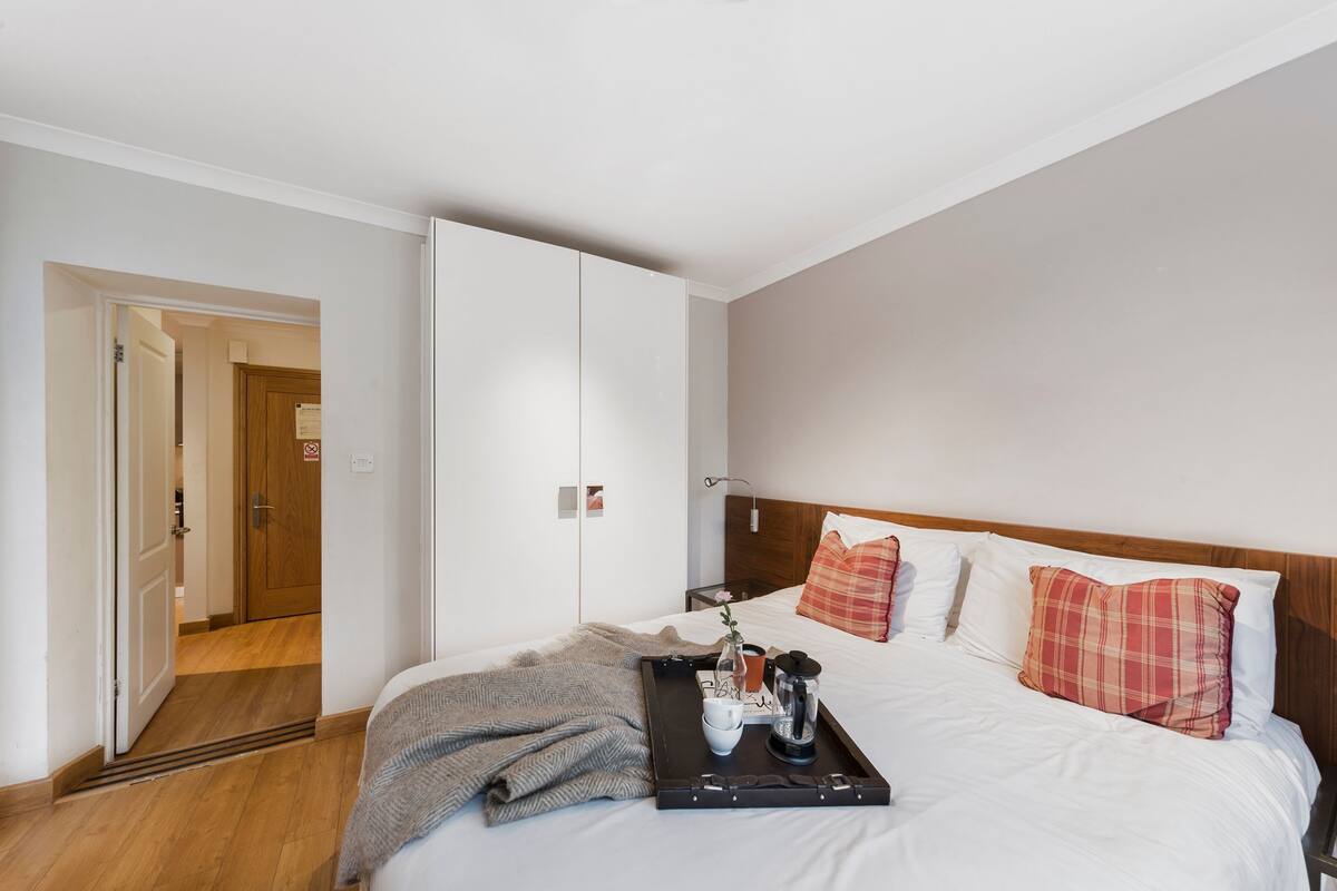 Une chambre d’hôtel avec un lit, un plateau contenant des articles pour le petit-déjeuner, une porte en bois et un mur blanc.