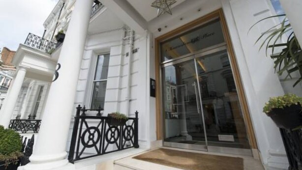 A building facade with a large glass entrance, white columns, and a star-shaped ceiling ornament. - Lux London South Kensington (London)