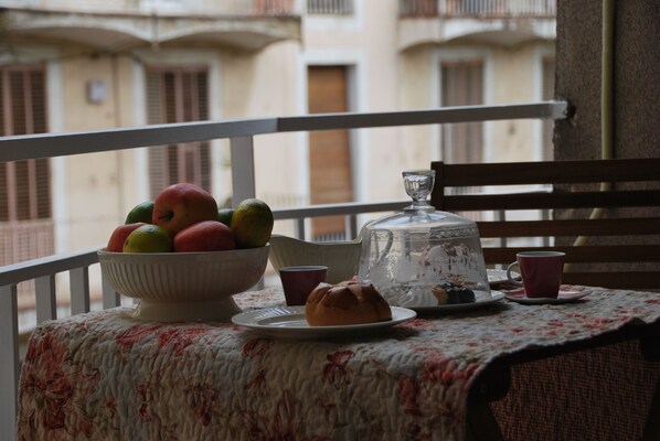A balcony with a table set for tea, featuring a floral tablecloth, a bowl of fruit, a teapot, and cups. - Apartment in the heart of Barcelona, Trafalgar-Urquinaona square (Barcelona)
