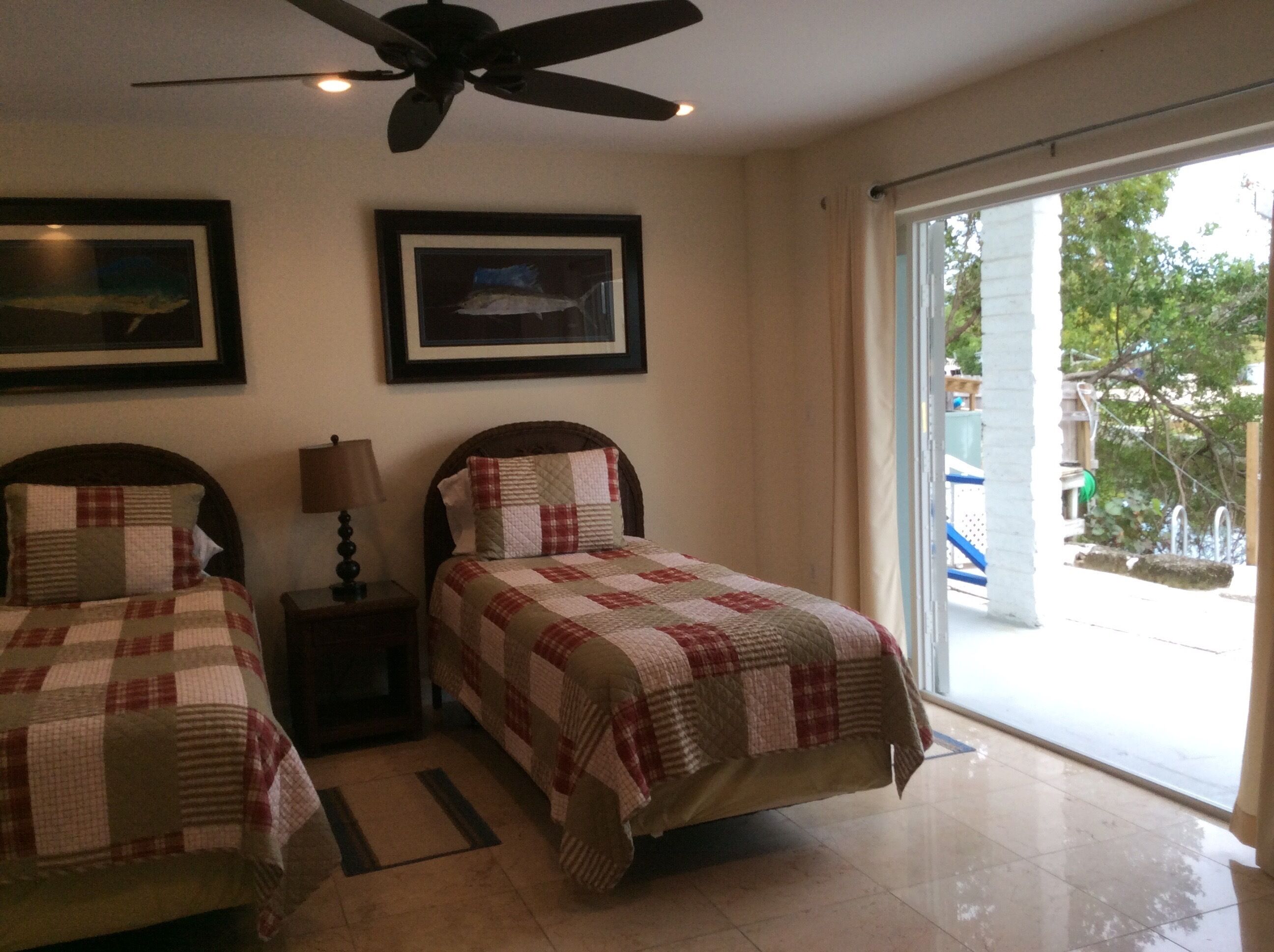 A bedroom with two beds, a ceiling fan, and a large window.