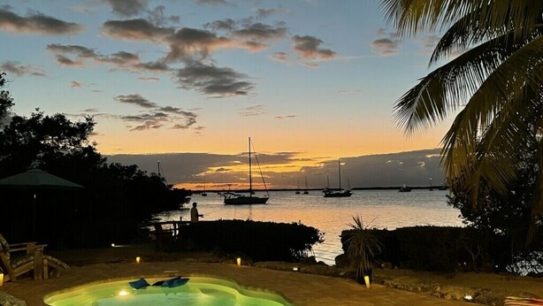 Ein Schwimmbecken mit Sonnenuntergangsblick, Booten auf dem Wasser und Palmen.