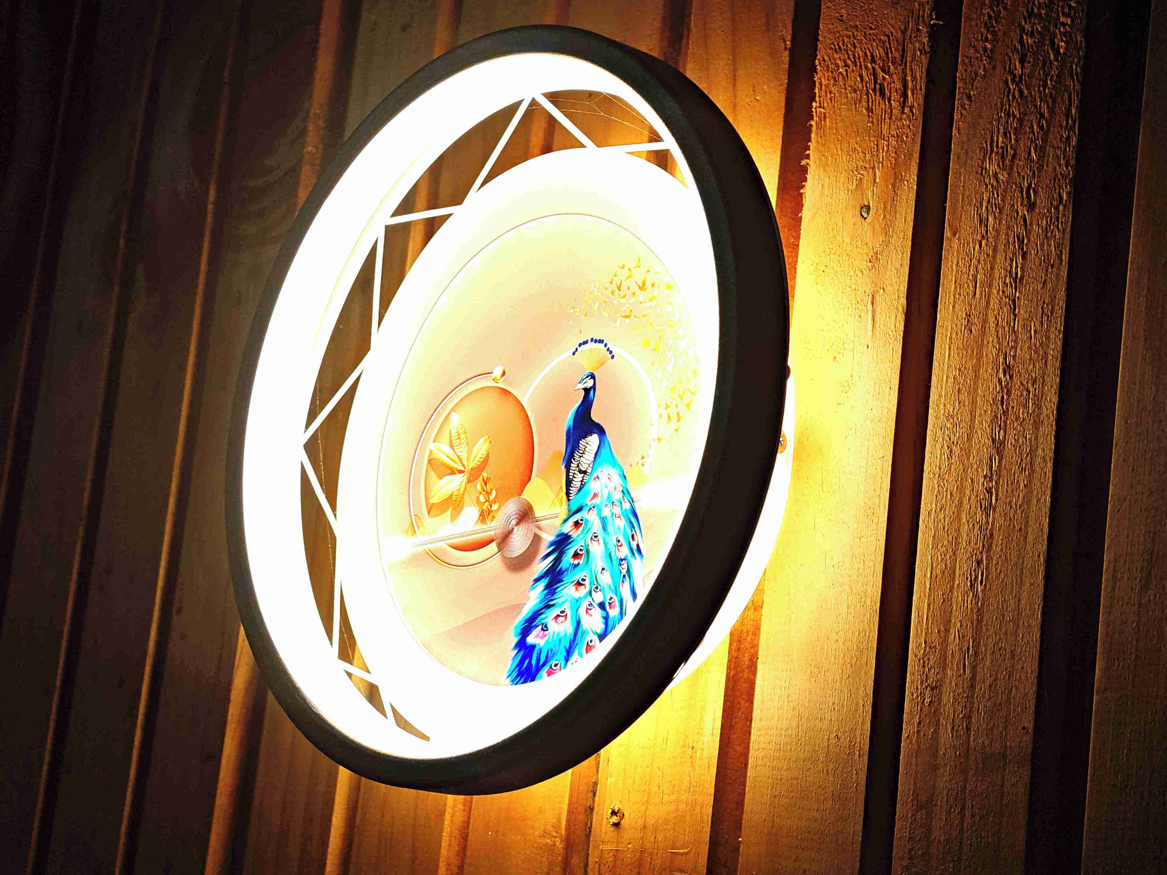 Lámpara circular con diseño de pavo real sobre una pared de madera.