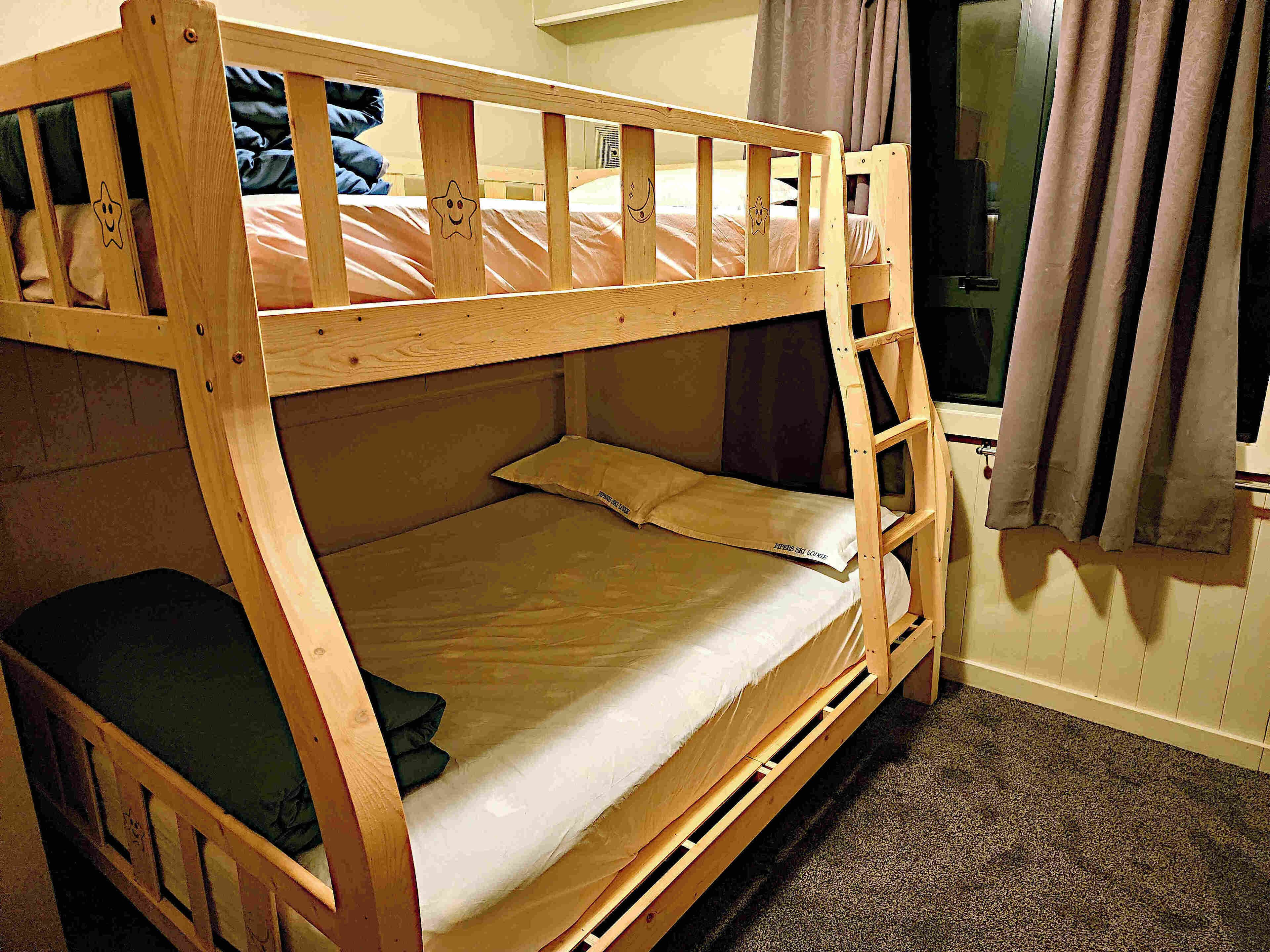 A bunk bed with a ladder, a window with curtains, and a carpeted floor.
