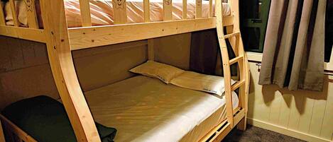 A bunk bed with a ladder, a window with curtains, and a carpeted floor.
