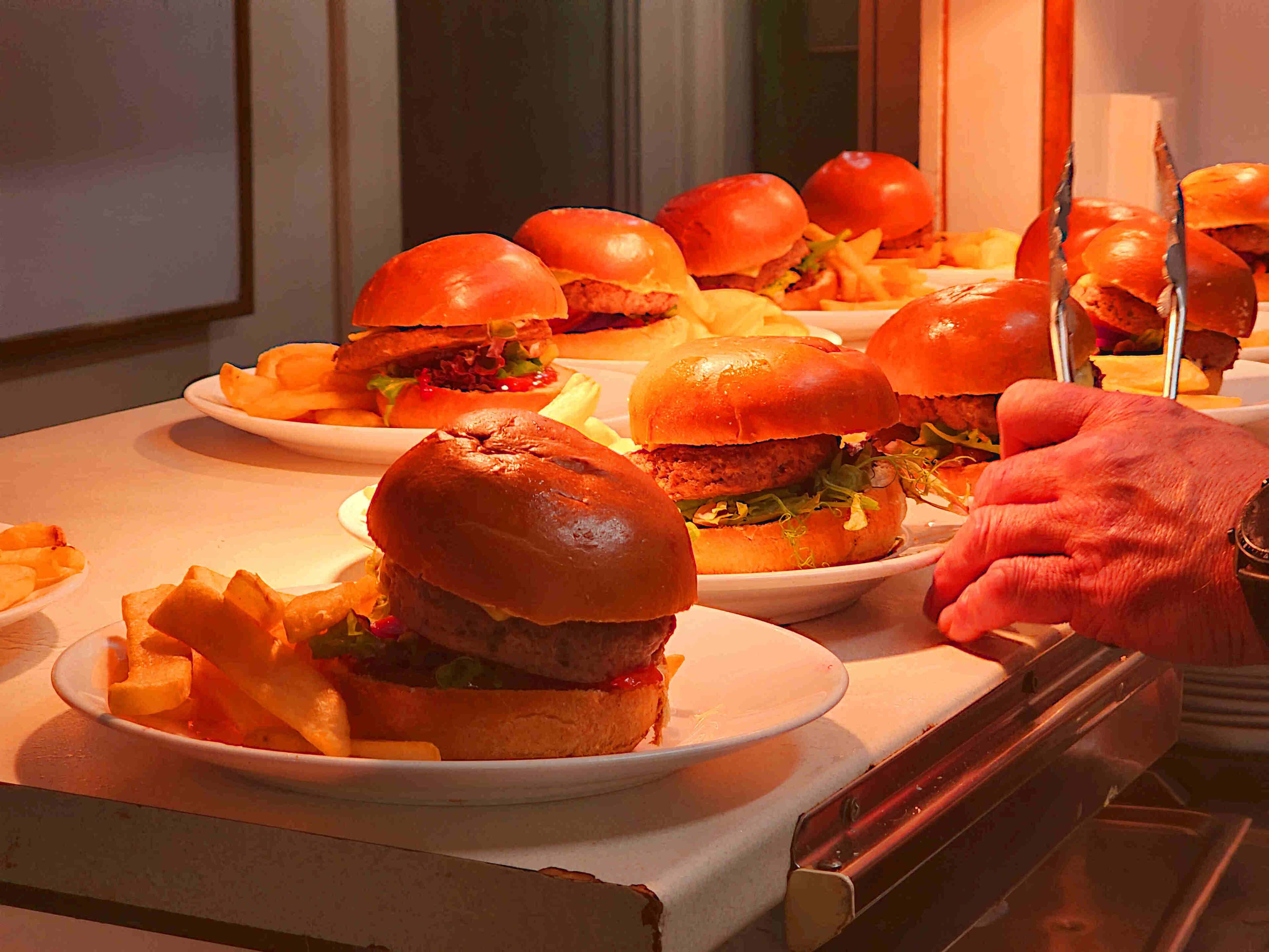 Une table de buffet avec des assiettes de hamburgers et de frites.
