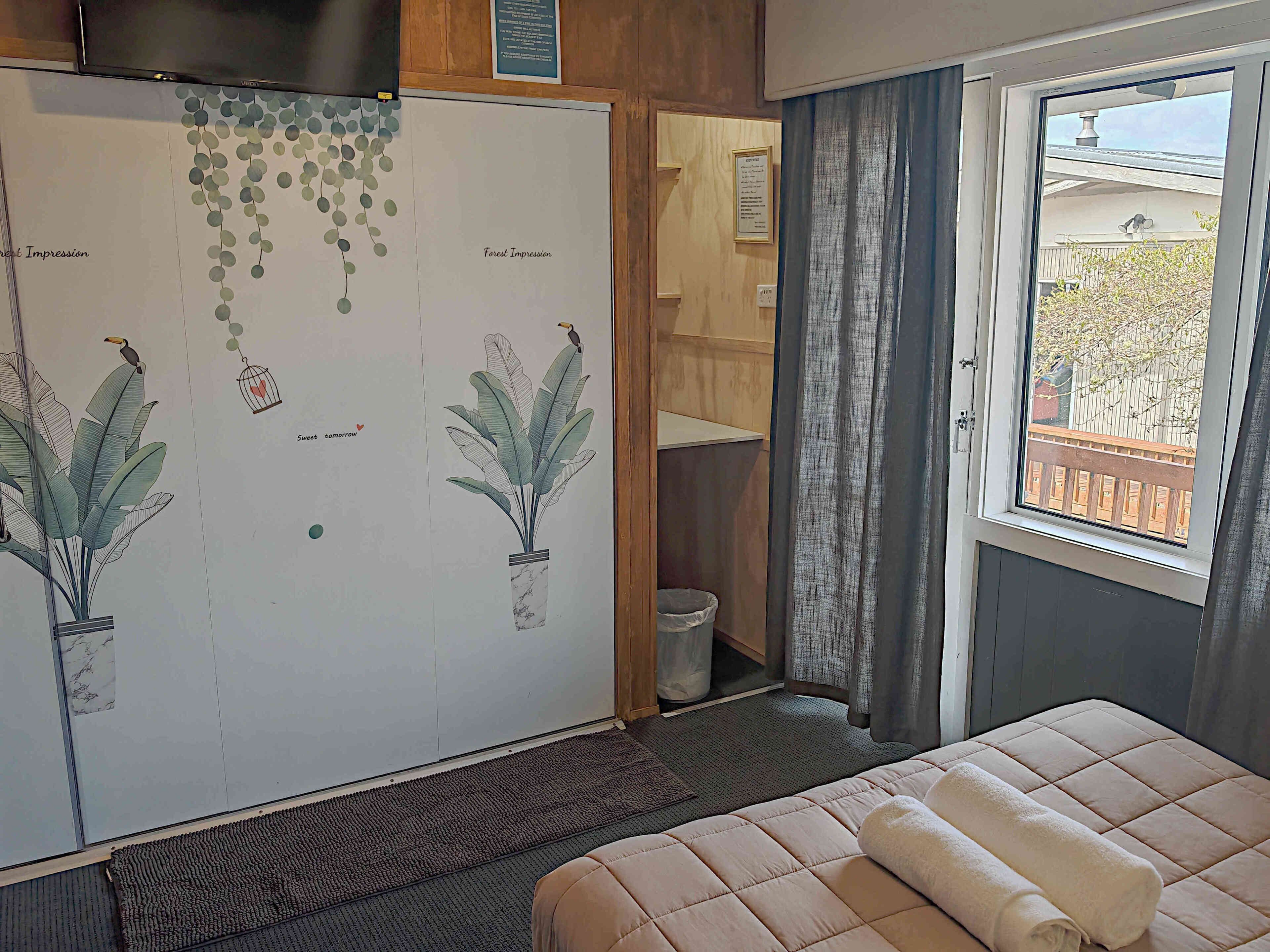 A bedroom with a bed, a window with a view, a door leading to a bathroom, and a wall with a decorative hanging.
