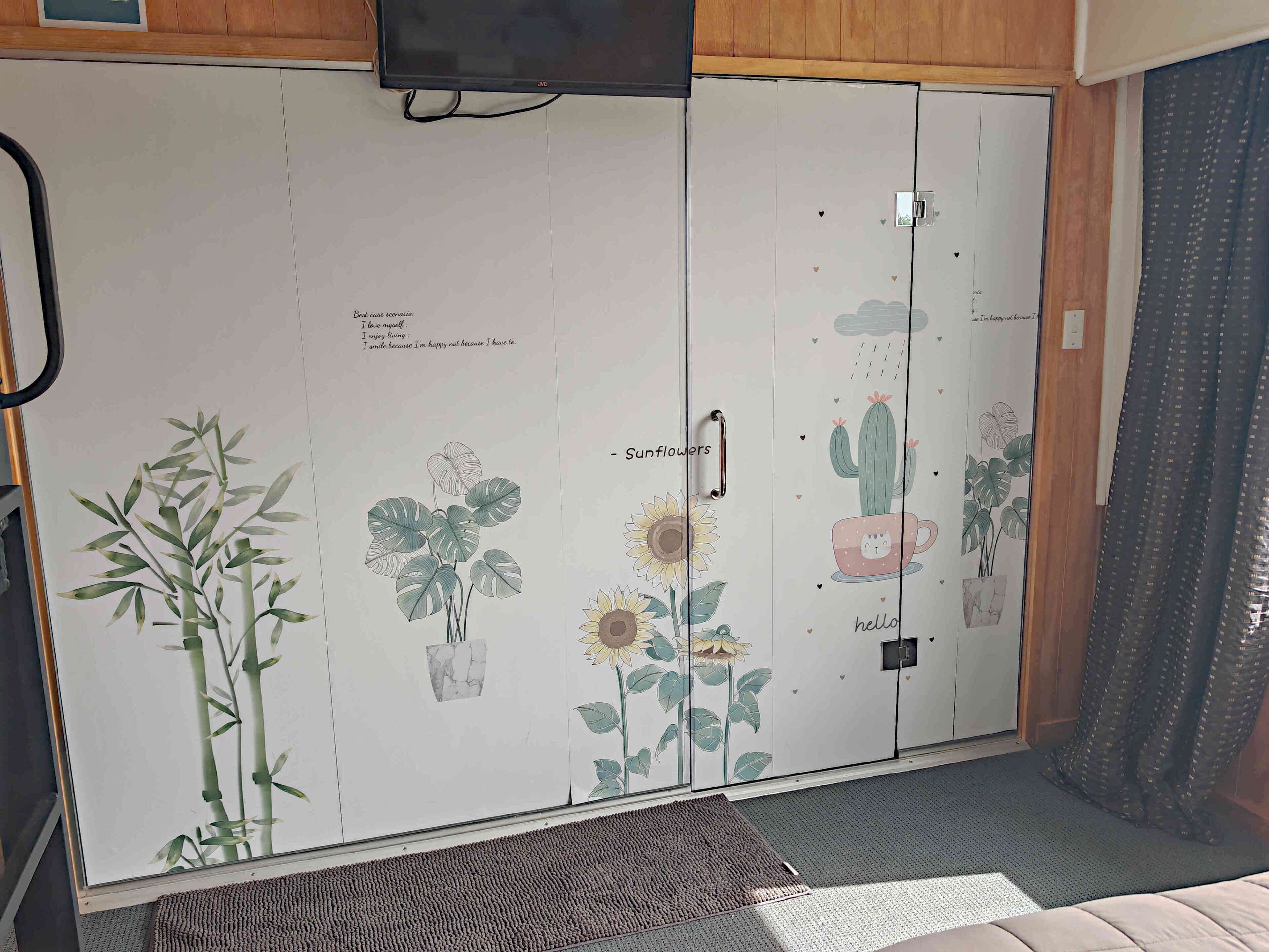 A room with a wardrobe featuring botanical illustrations and a television mounted above it.