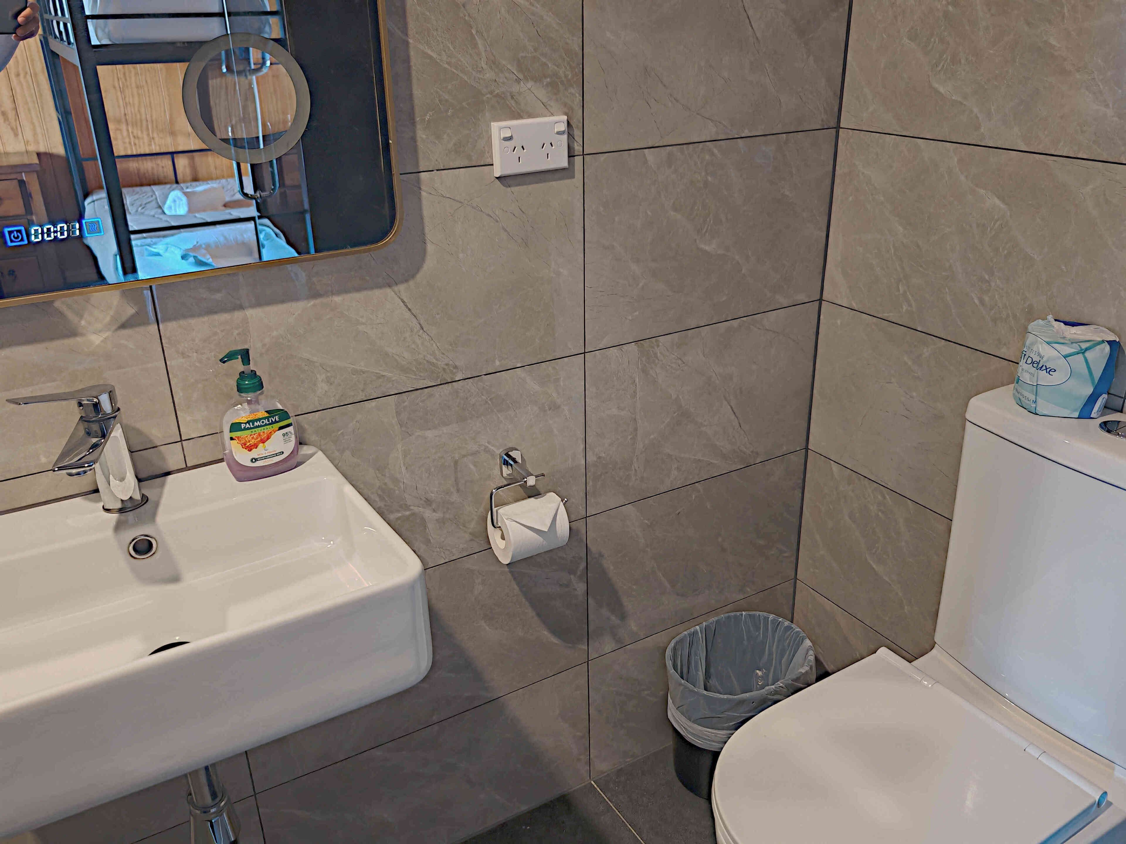 A bathroom with a white sink, a mirror, a toilet, and a trash bin.